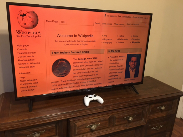 TCL TV set on stand on dresser, HDMI-connected to Windows computer, the blue light filter on, on WP homepage, with XB1 controller a remote input device Bluetooth-connected to the PC, which uses Controller Companion
